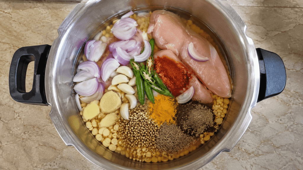 Chicken breast, soaked chana dal and spices placed in a pressure cooker before cooking.