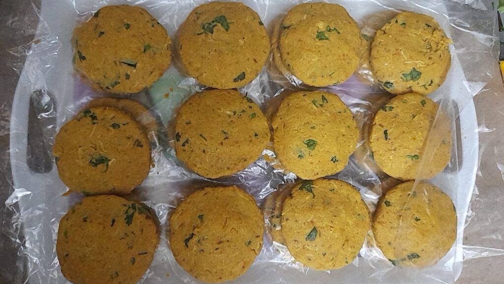 Homemade Chicken Shami Kababs arranged in layers on tray with plastic sheets before freezing.